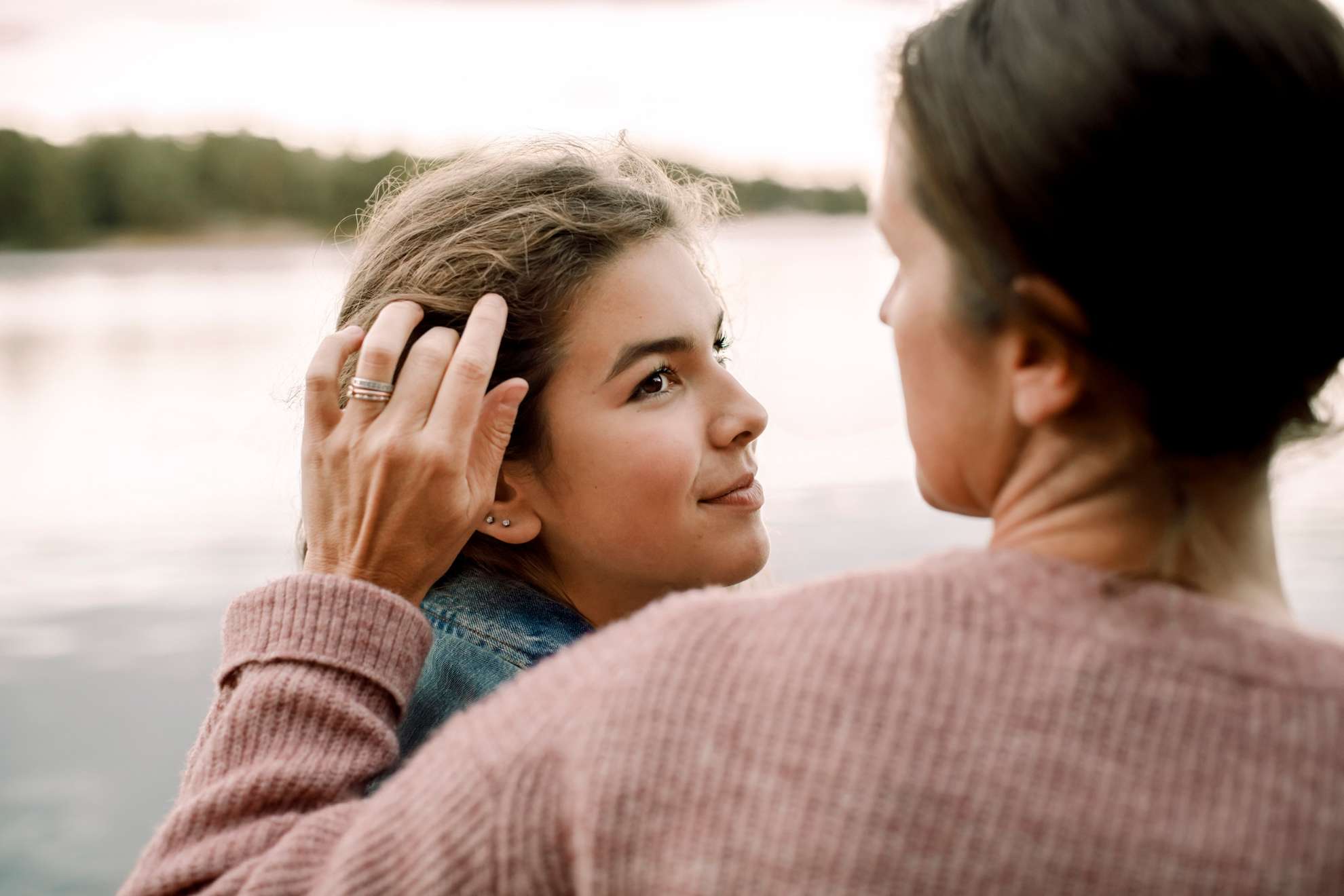 En kvinna står tätt intill en liten flicka och stryker flickans hår bakom örat.