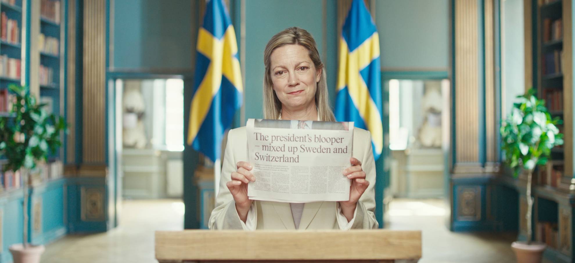 Kvinna håller upp en dagstidning. Bakom henne syns två Sverigeflaggor.