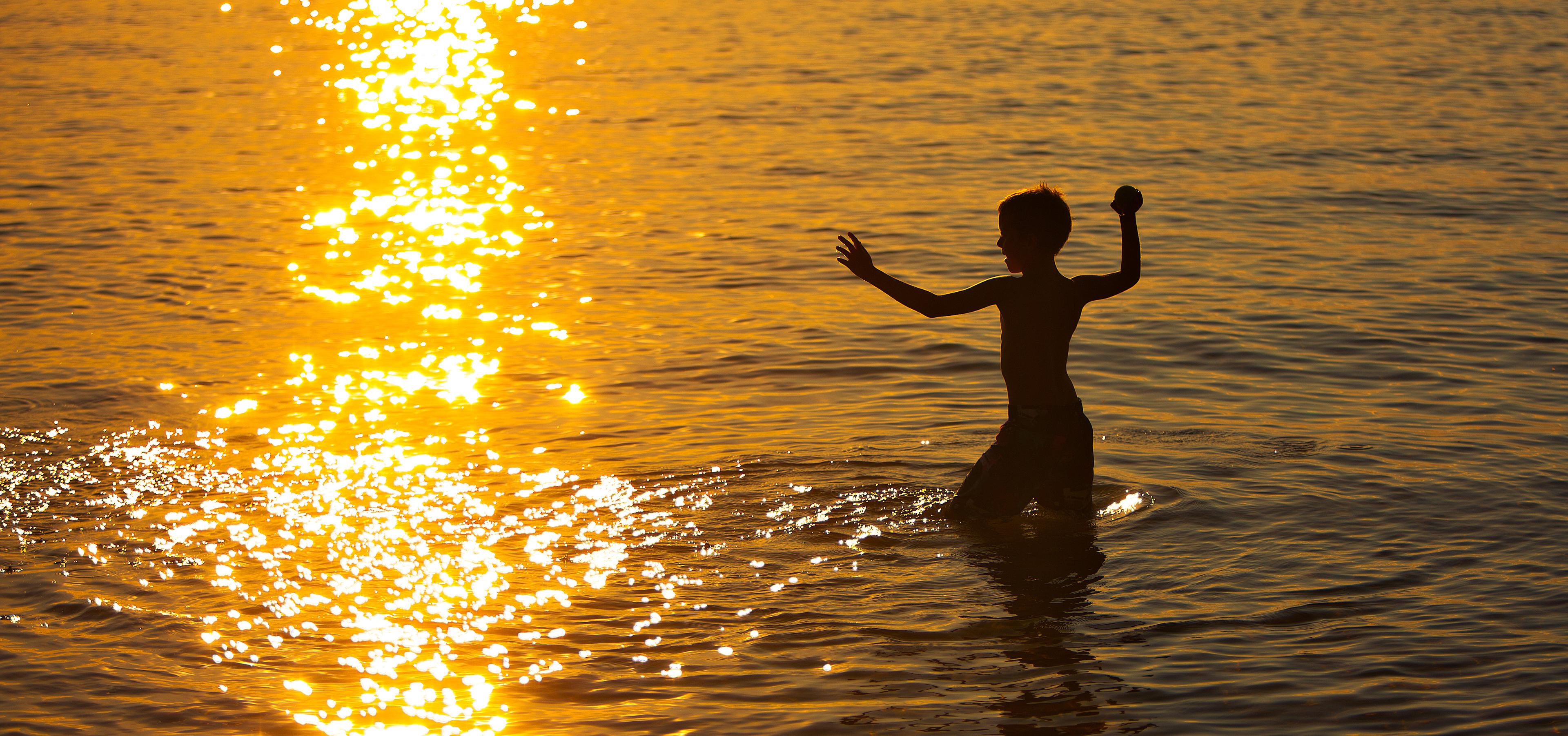 Ett barn leker i vattnet i solnedgången.