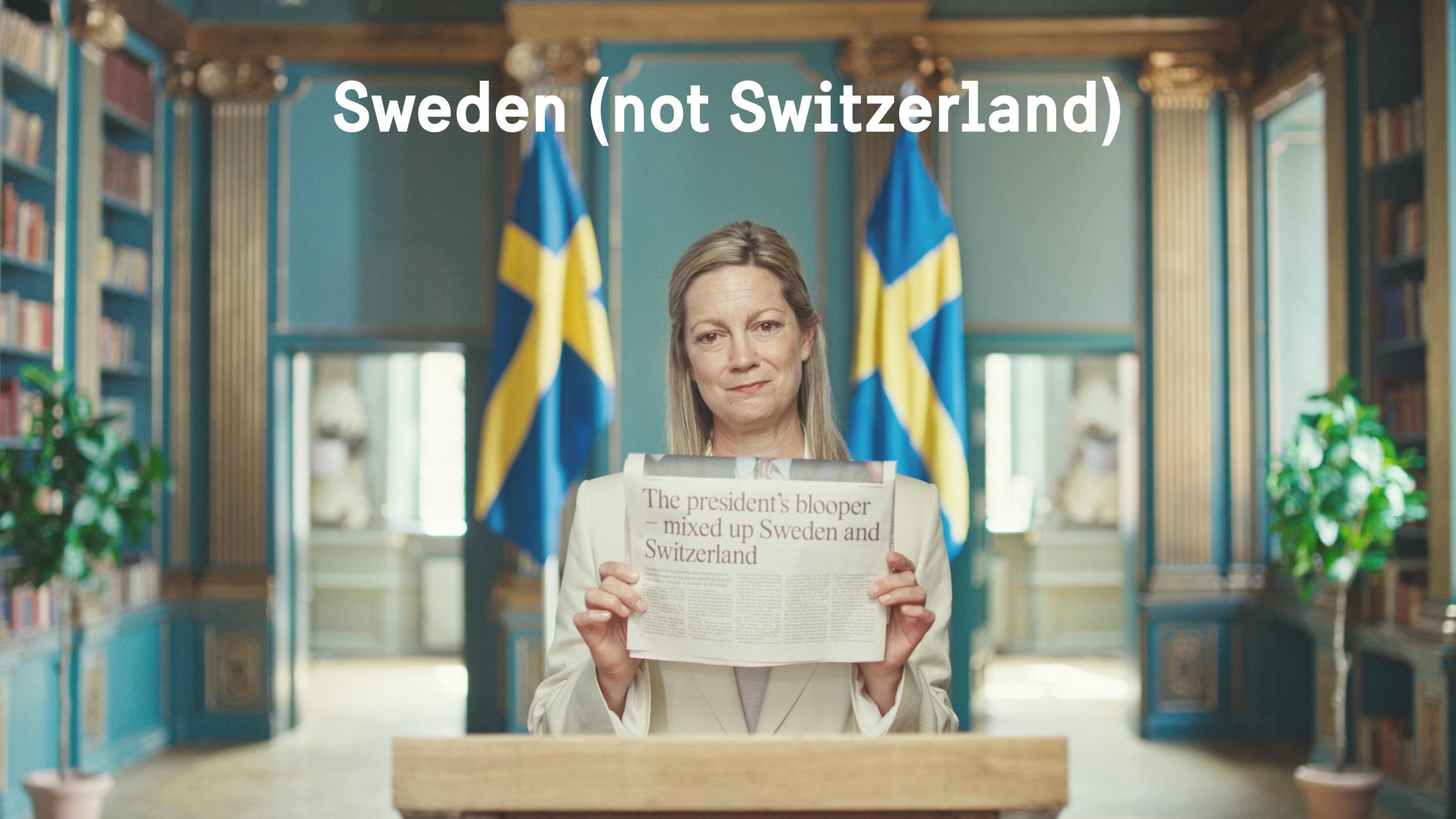 Kvinna står och håller fram en tidning som visas i bild. Text i bild som säger Sweden (not Switzerland).