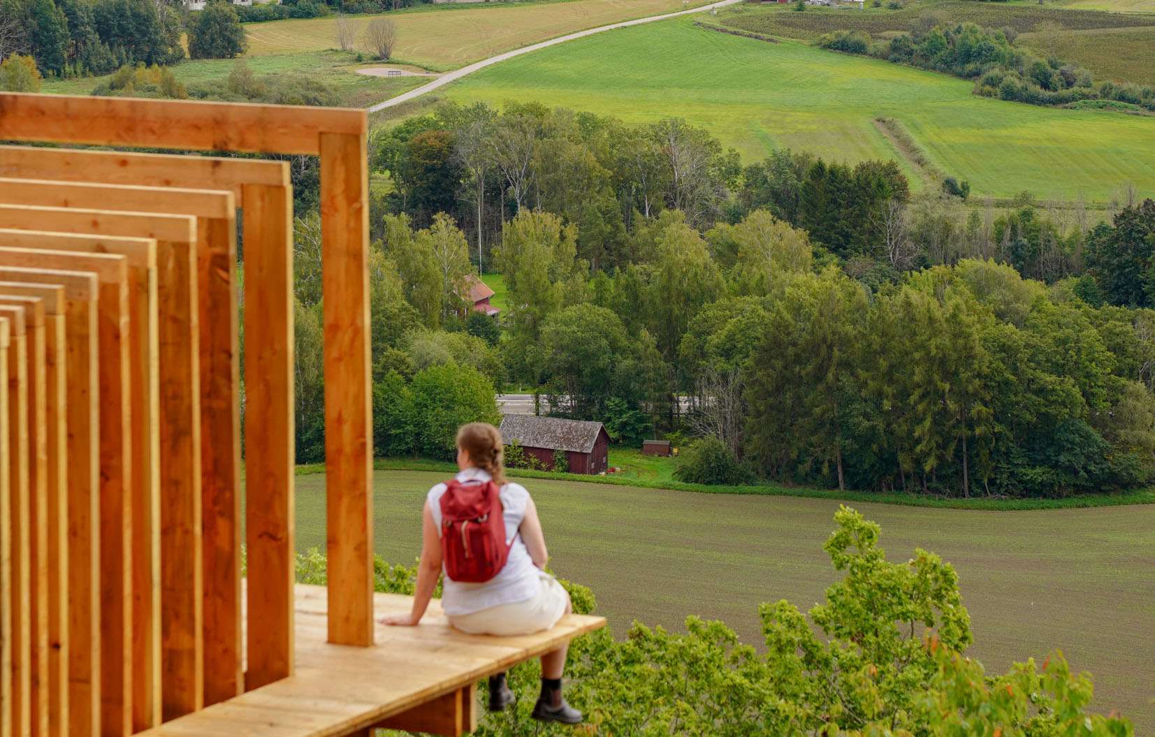På en utskjutande träavsats sitter en person och blickar över ett helt landskap nedanför.