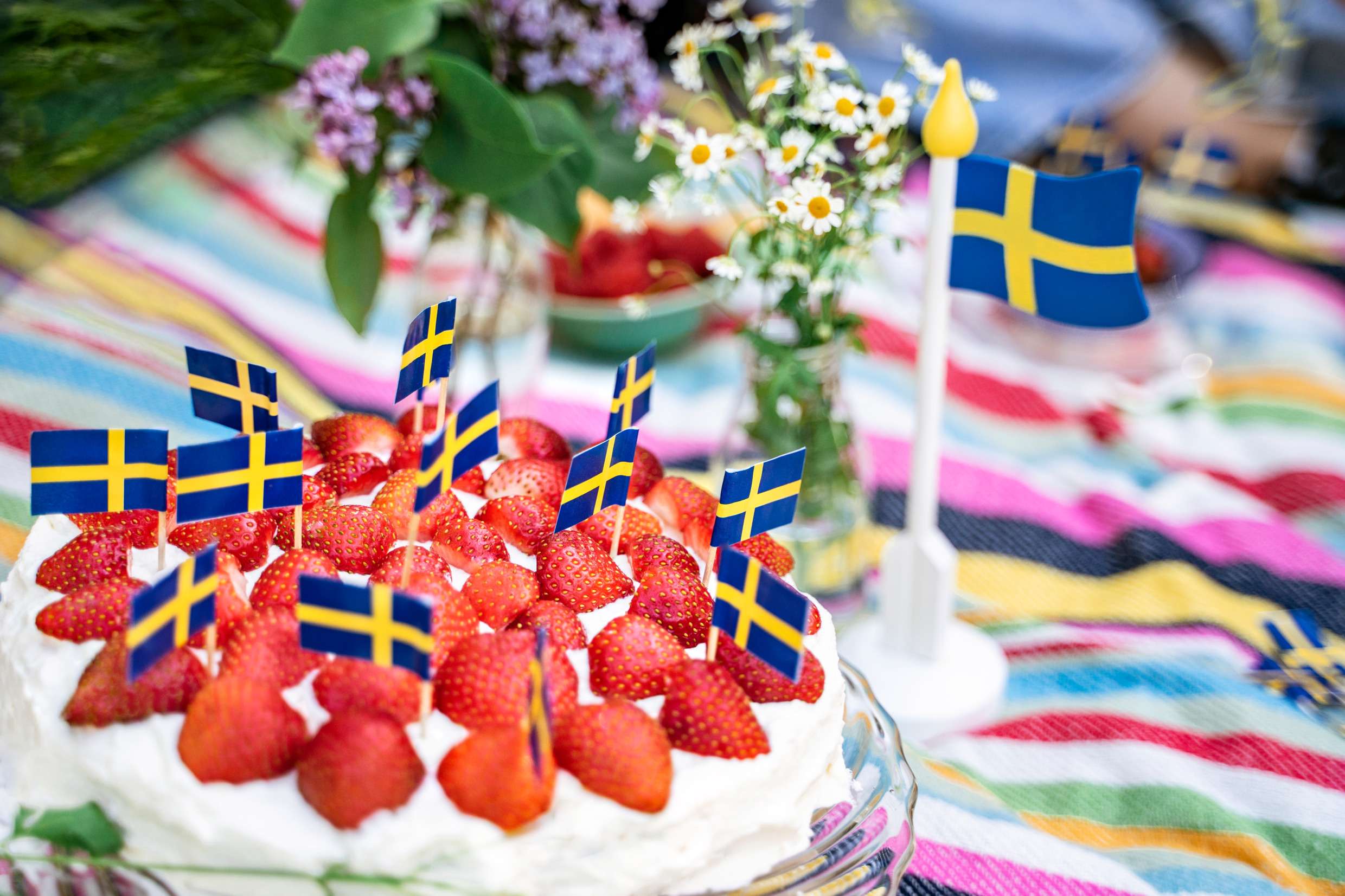 En jordgubbstårta på ett sommardukat bord med en svensk flagga.