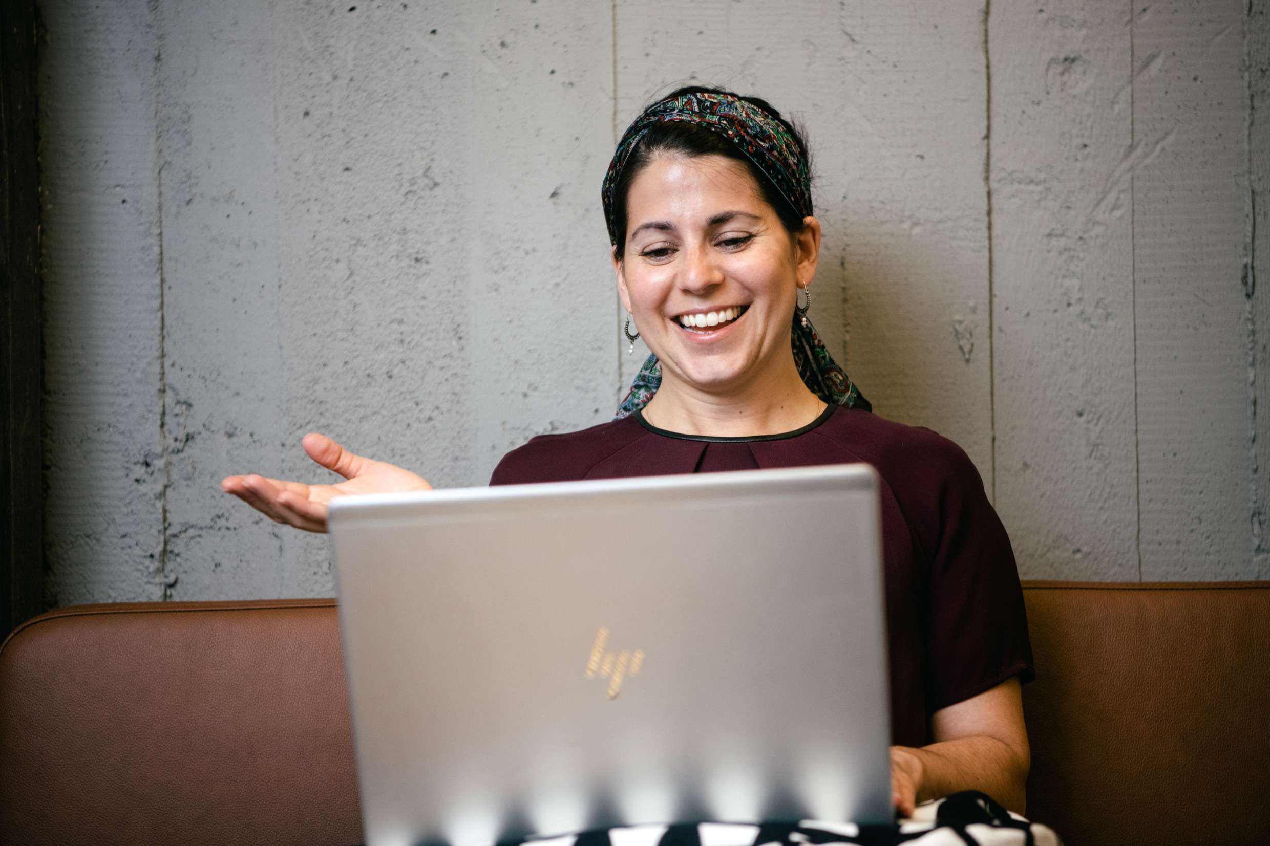 En kvinna sitter framför en dator, skrattar och håller upp ena handen.