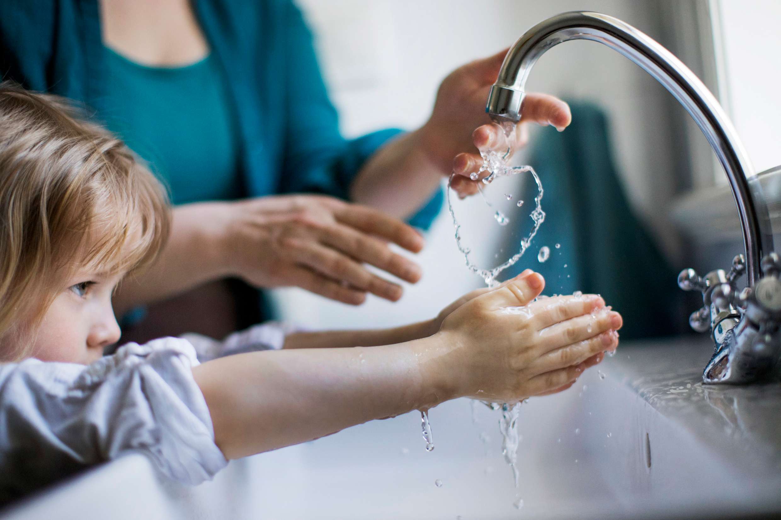 En liten flicka står bredvid en vuxen kvinna och tvättar händerna under kranen.