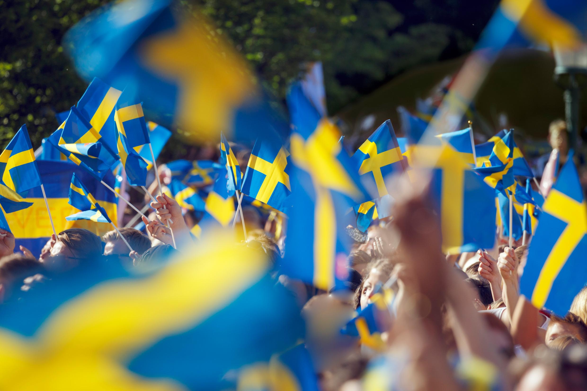 Bilden visar ett hav av svenska flaggor viftandes av en folkmassa.