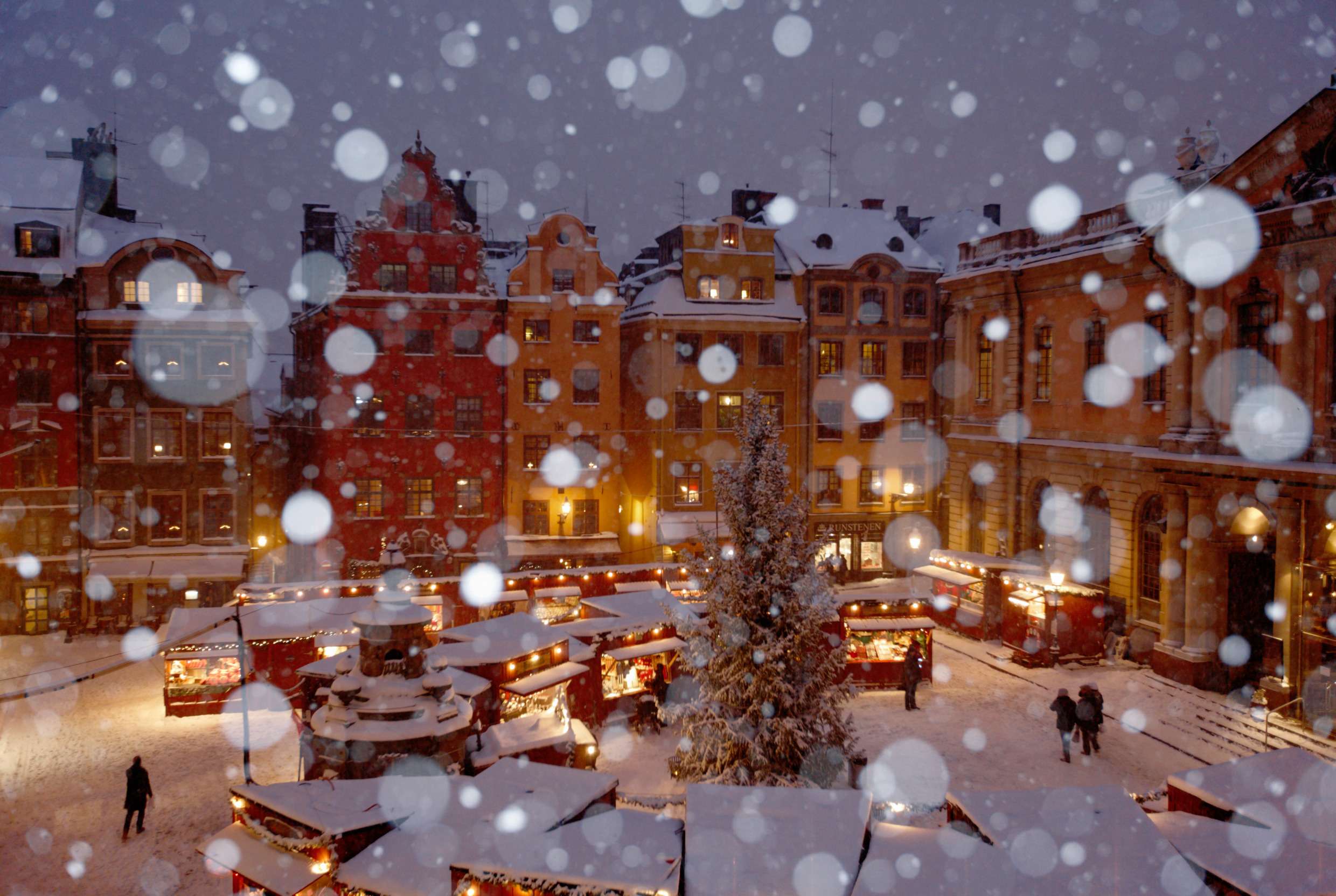 En flygbild över ett snöigt stora torget i Gamla Stan i Stockholm. På torget pågår full aktivitet i alla bodar som står uppställda för julmarknaden.