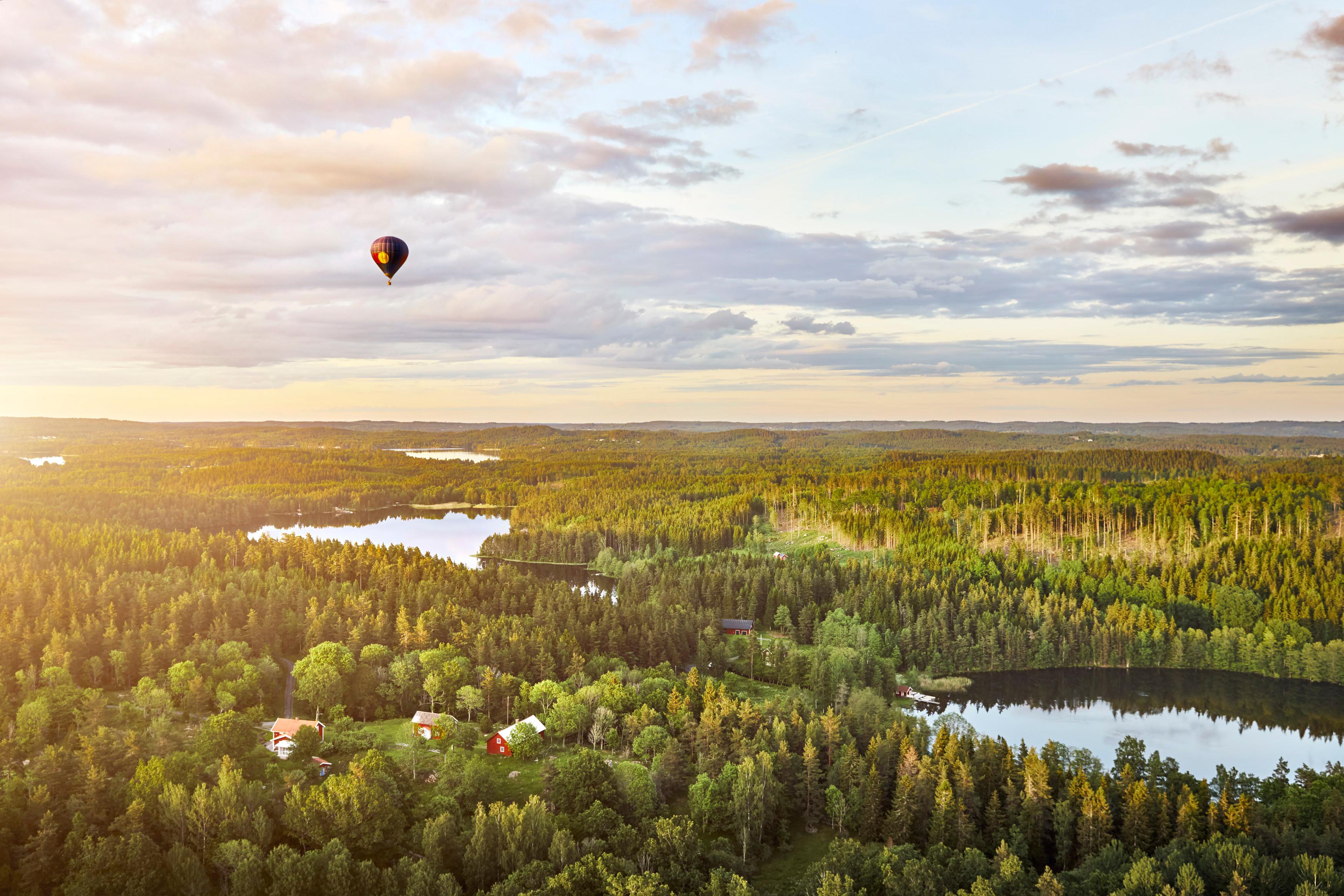 En luftballong högt i luften över skog, sjöar och några få hus.