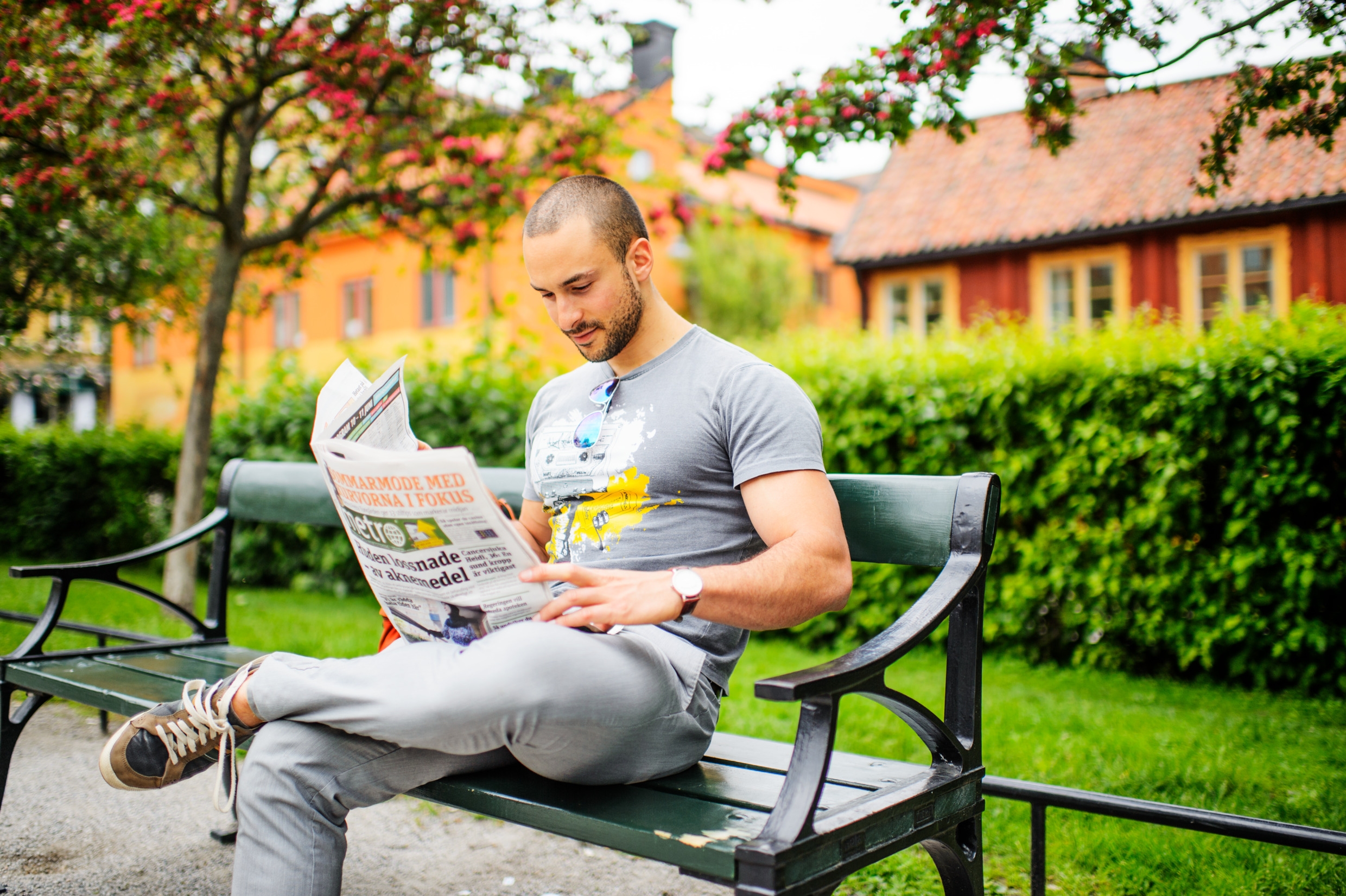 En man sitter utomhus på en parkbänk och läser en tidning.