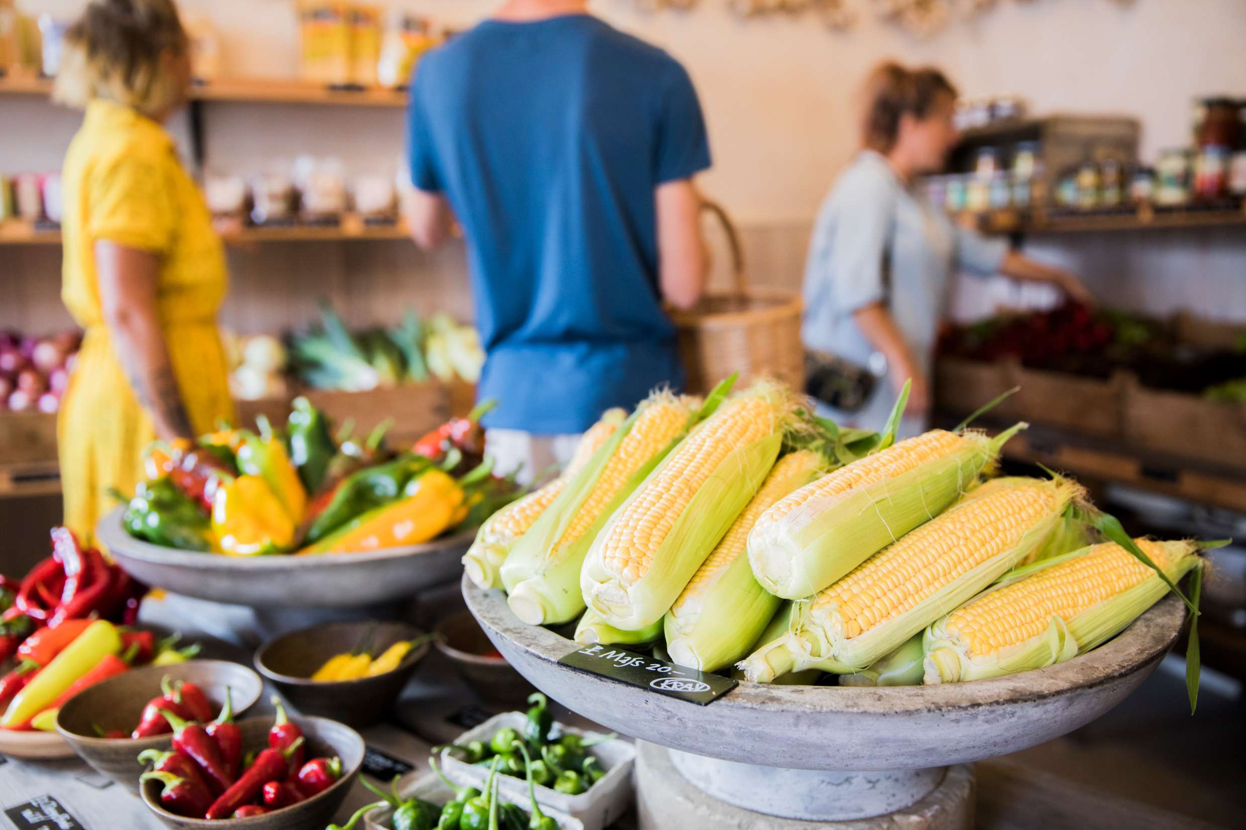Ett stort fat med majs i förgrunden och en mängd fat med grönsaker i en liten försäljningslokal på Gotland.